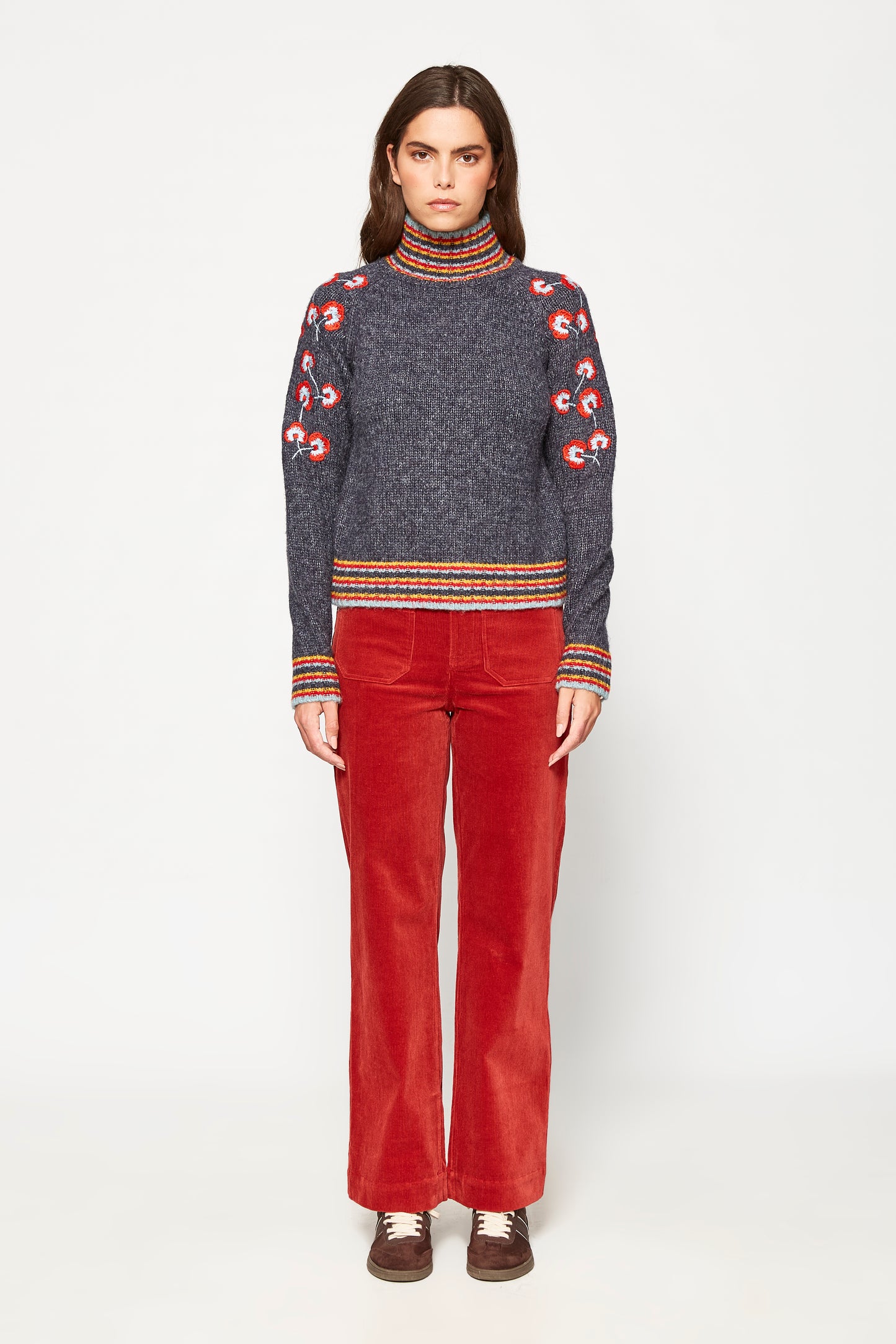 Woman wearing a patterned sweater and red pants on a white background
