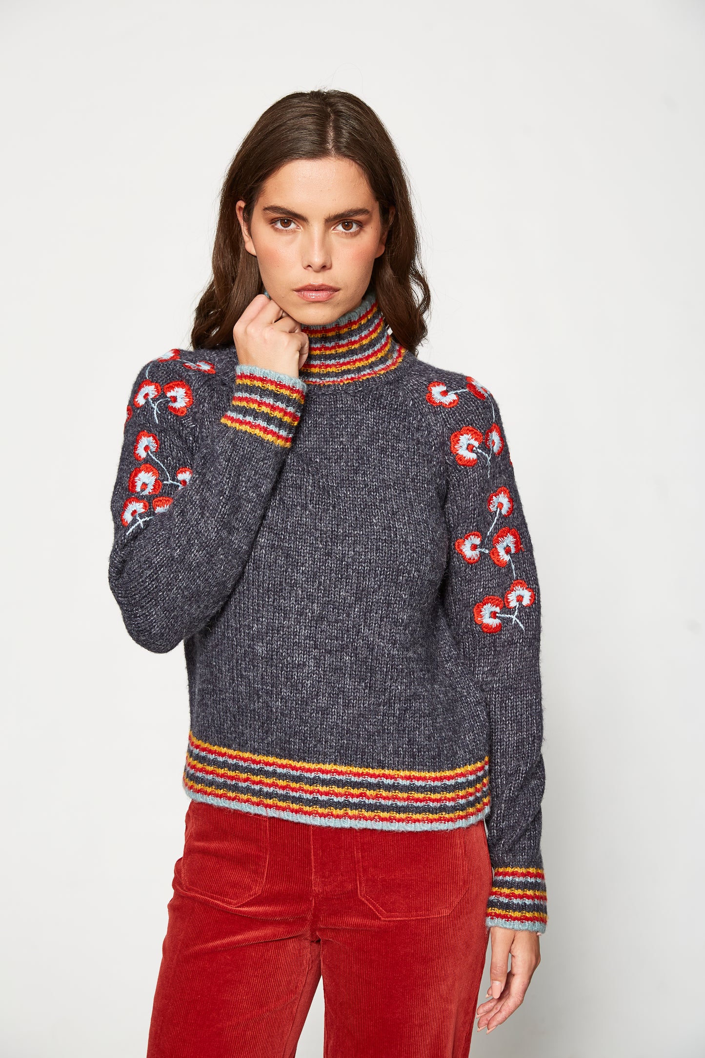 Woman wearing a dark gray sweater with colorful patterns and red pants on a white background