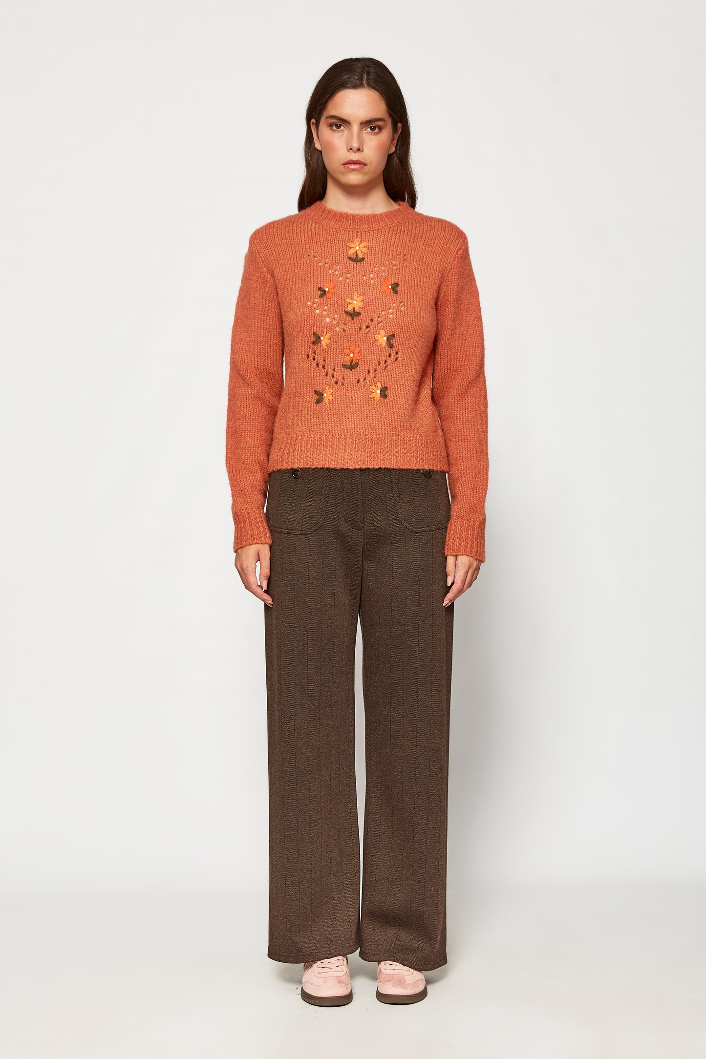 Woman wearing a brown sweater with a pattern and brown pants on a white background