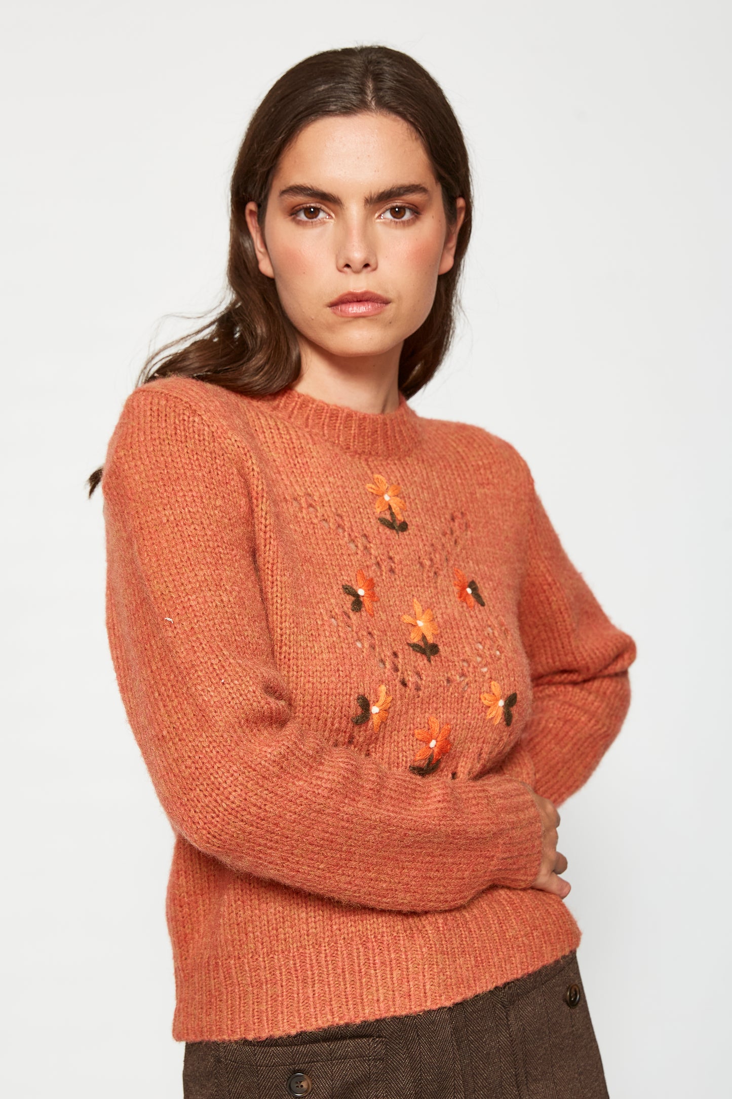 Woman wearing a brown sweater with embroidered designs on a white background