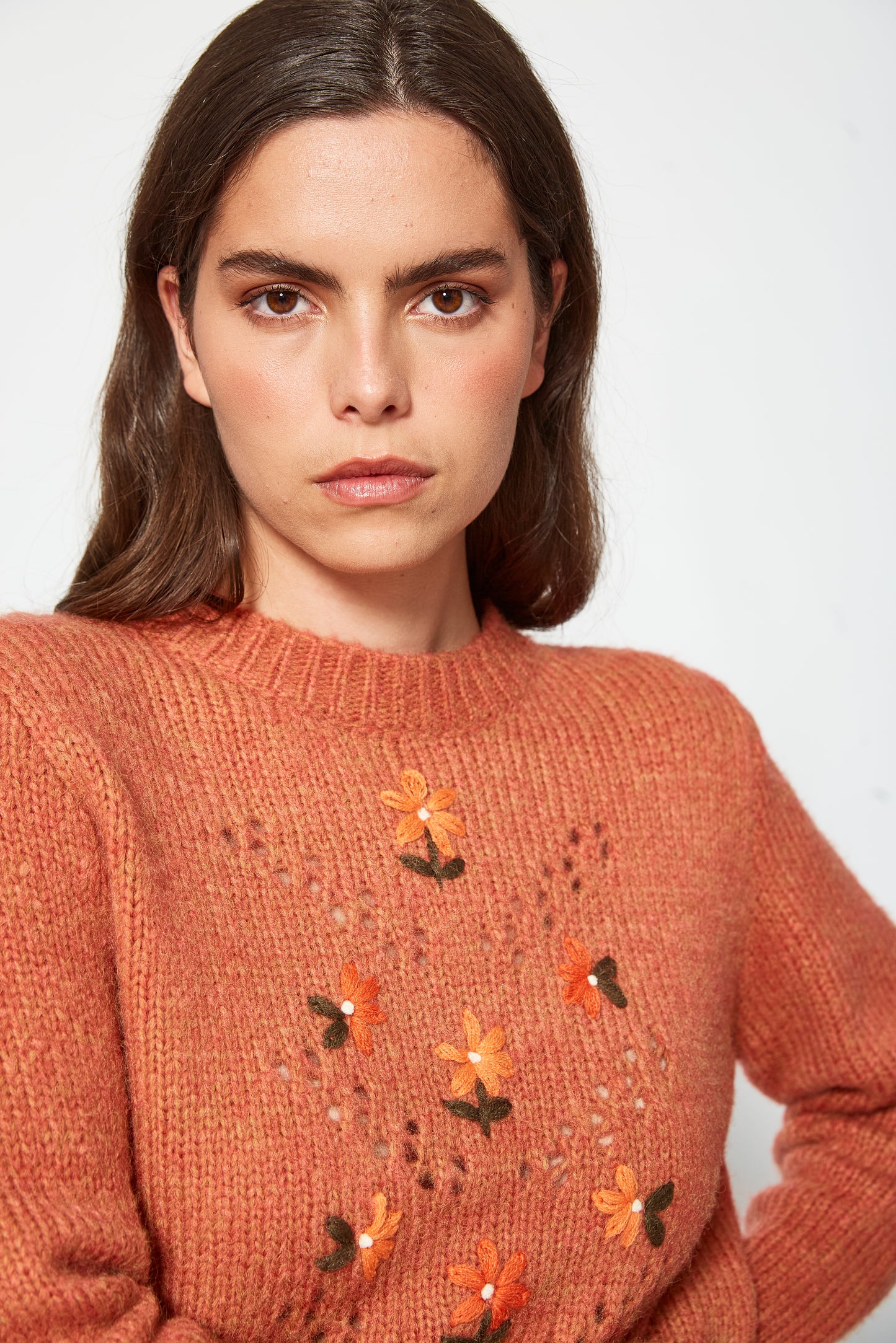 Woman wearing a brown sweater with floral patterns on a white background