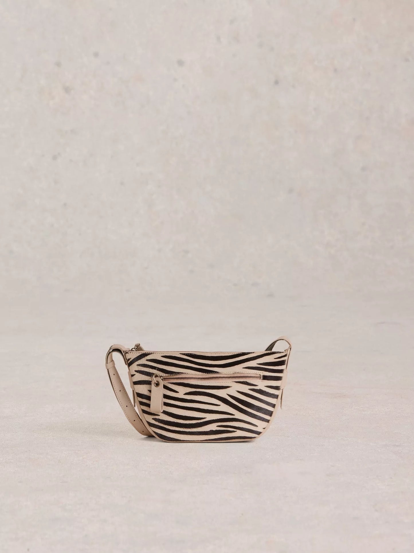 the Caro Crossbody Bag from White Stuff. Its crescent shape is updated for a modern twist. You'll be delighted by the multitude of zippered pockets and an adjustable strap for the perfect fit. Plus, who can resist the abstract zebra print in luxurious calf hair?