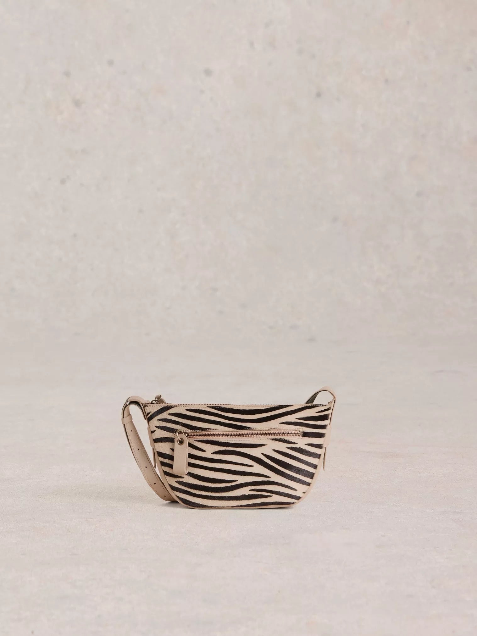 the Caro Crossbody Bag from White Stuff. Its crescent shape is updated for a modern twist. You'll be delighted by the multitude of zippered pockets and an adjustable strap for the perfect fit. Plus, who can resist the abstract zebra print in luxurious calf hair?