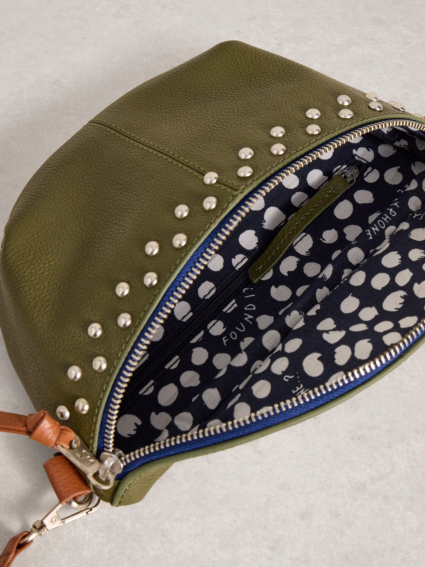 Green studded pouch with a navy interior featuring white polka dots on a light gray background