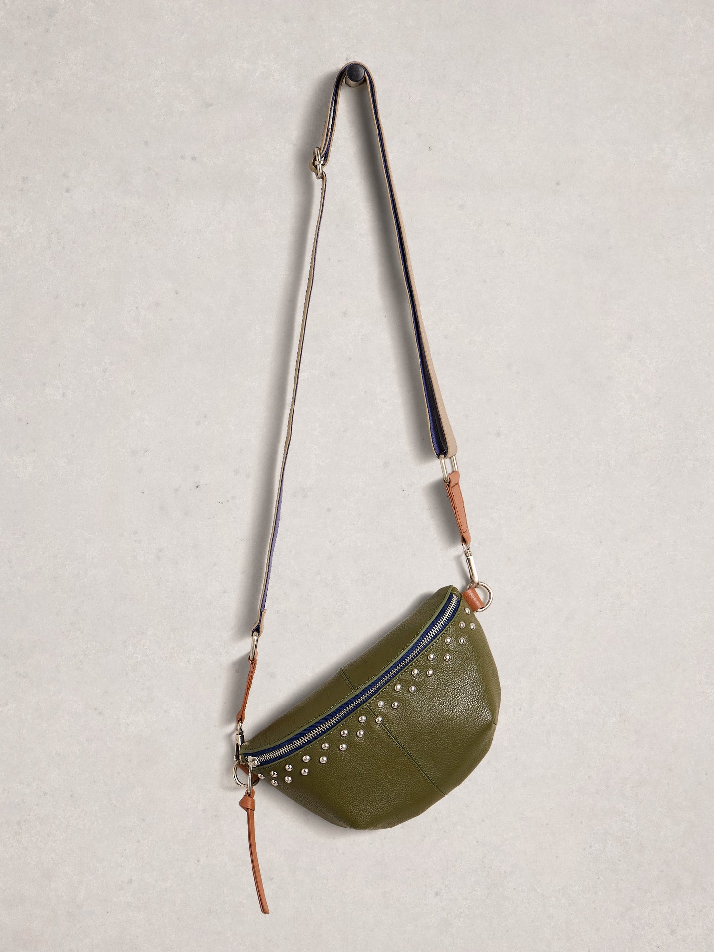 Green crossbody bag with studded details on a light gray background