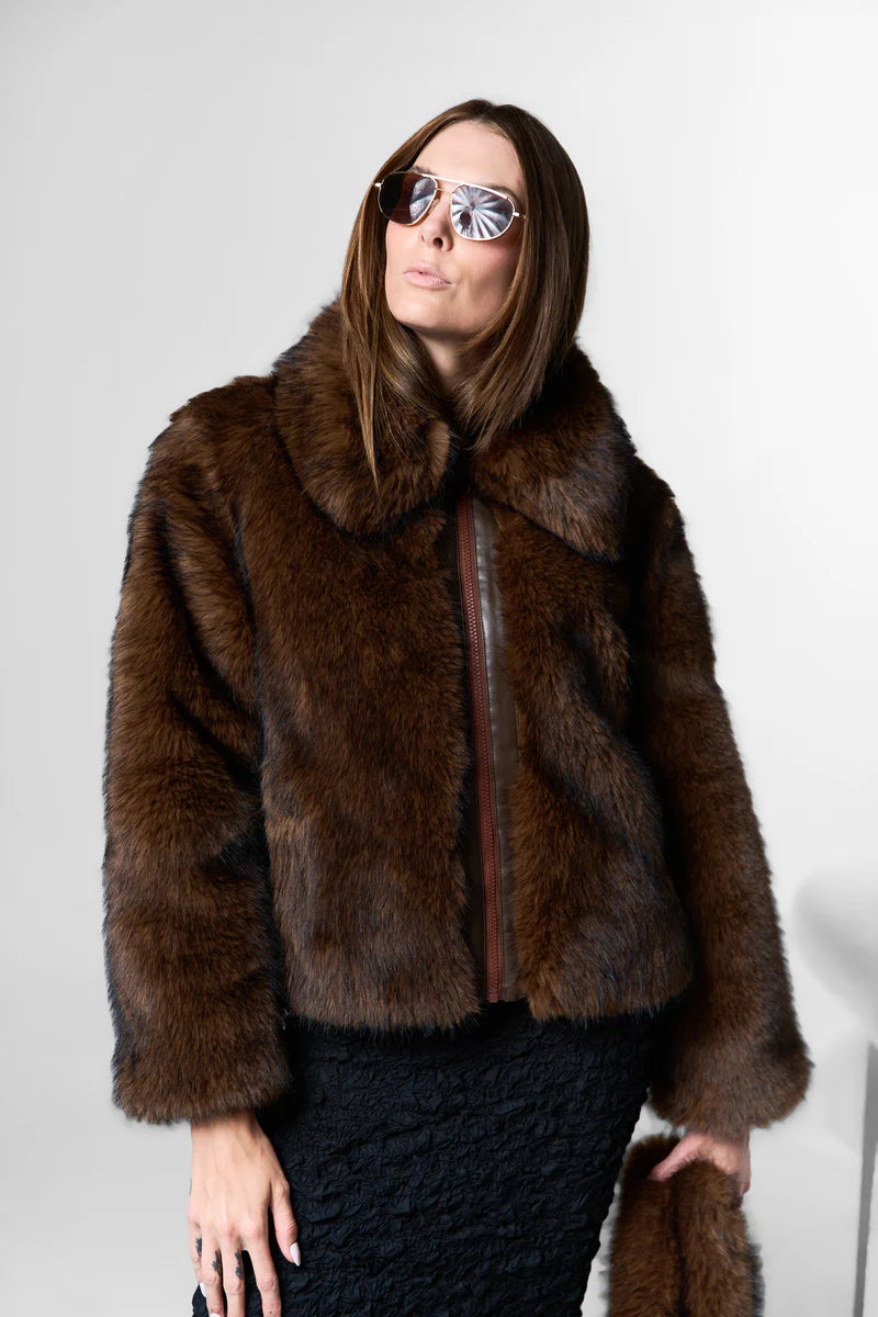 Woman wearing a brown fur coat and sunglasses against a white background