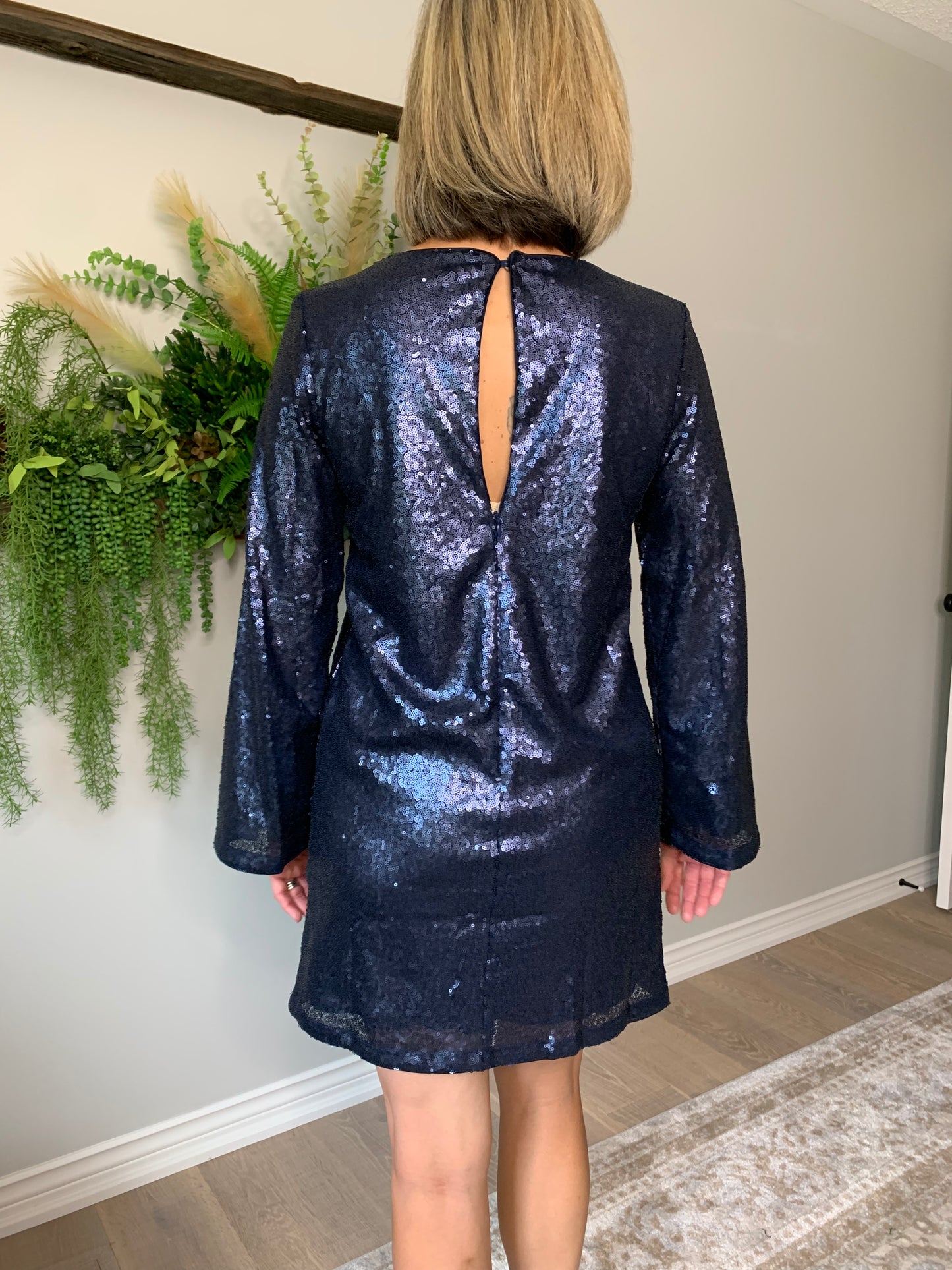 Be the star of the show with the Kelsey Dress by FRNCH! This stunning dress features marine blue sequins to ensure you sparkle in any setting, along with long sleeves to combat cooler temperatures and add an elegant touch. An above the knee length strikes the perfect balance between classic and classy, complemented by a subtle back peep hole detail that adds a hint of mystery.