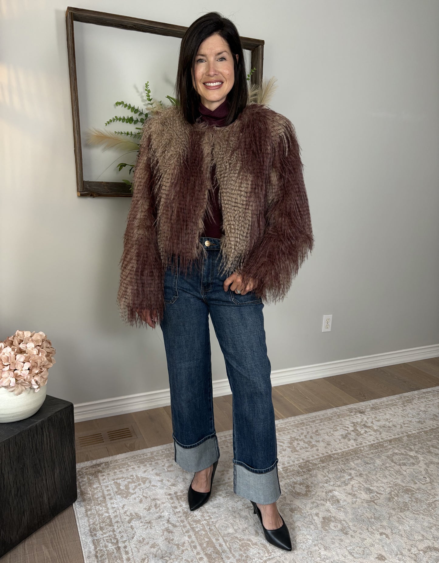 Woman wearing a brown fur coat and blue jeans indoors.