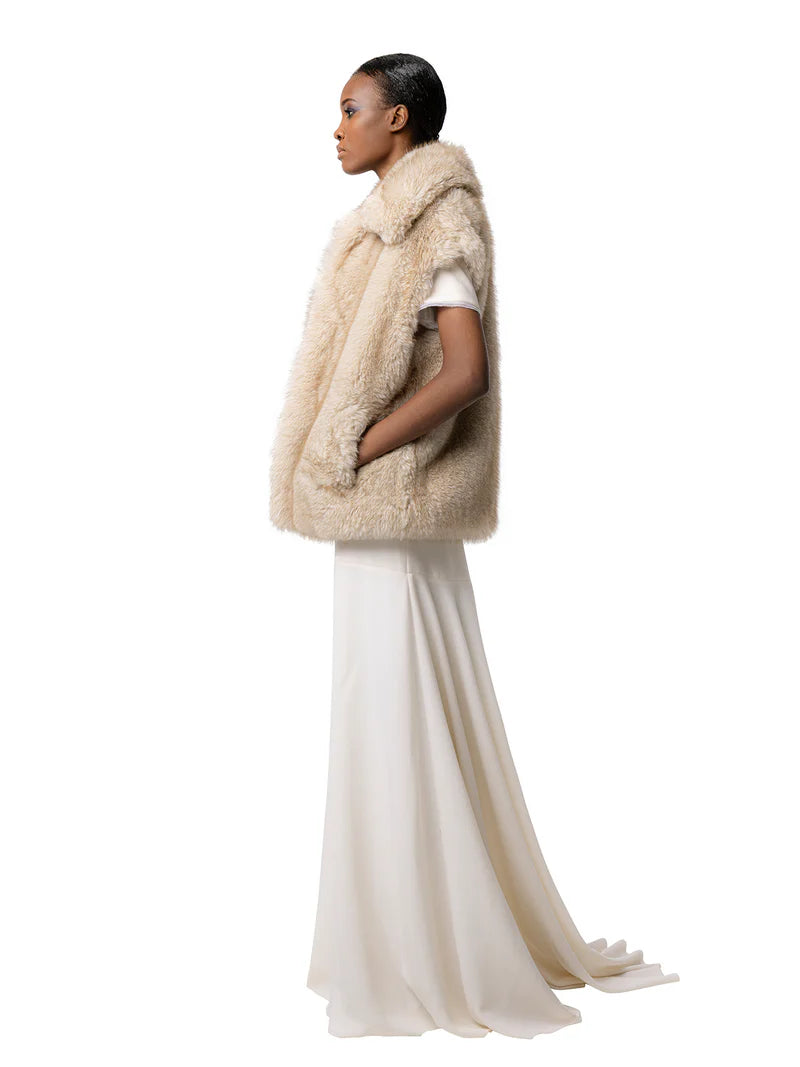 Woman wearing a beige fur vest over a white outfit on a white background