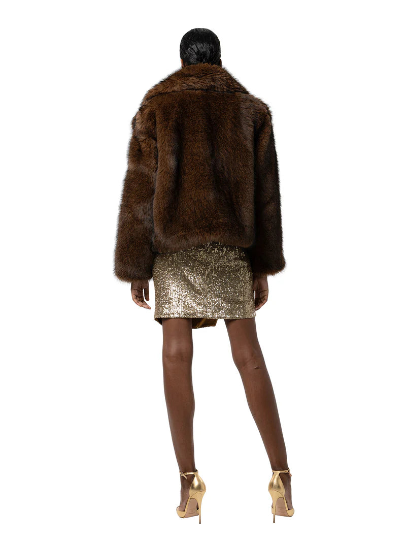 Person wearing a brown fur coat and gold sequin skirt on a white background