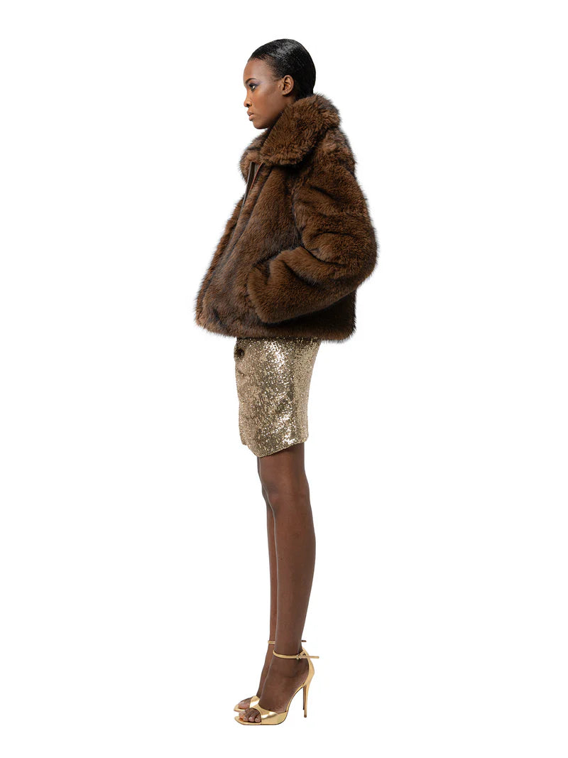 Woman wearing a brown fur coat and gold sequin skirt on a white background