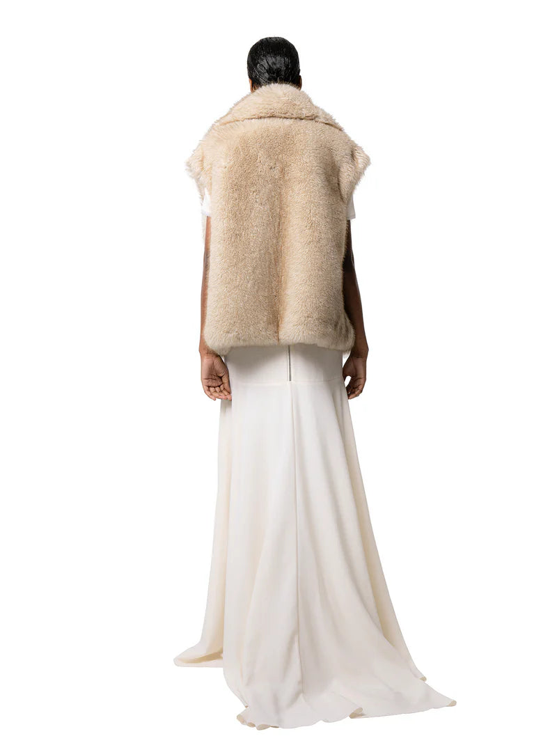 Person wearing a beige fur vest and white pants on a white background