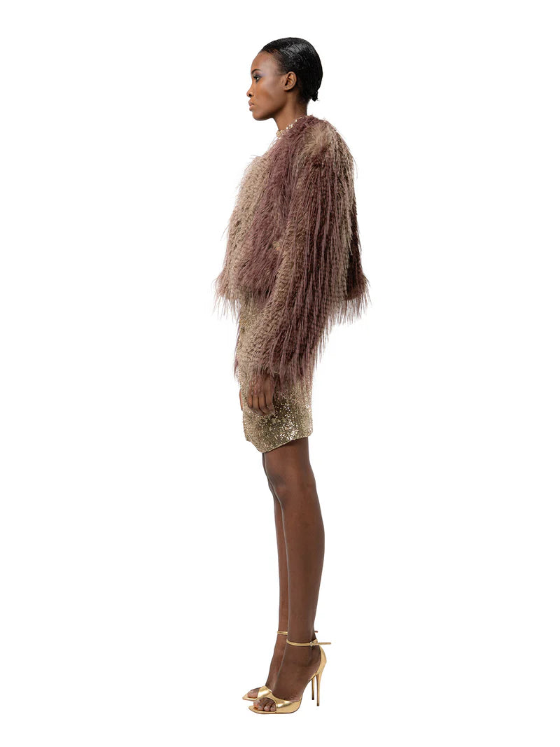 Woman wearing a textured brown jacket and gold dress on a white background