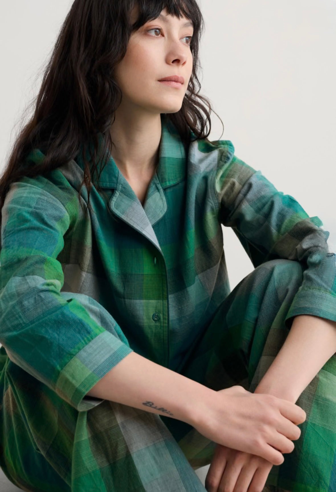 Woman wearing a green plaid outfit sitting against a plain background