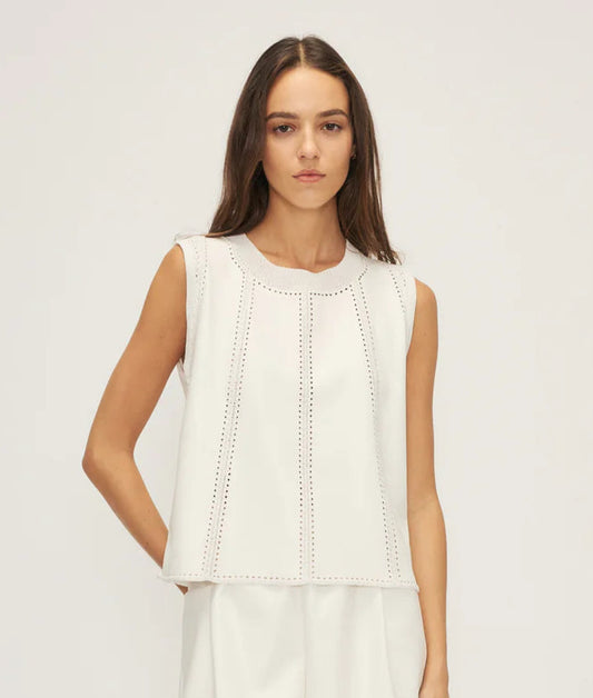A female model wearing a white faux leather and crochet top with tailored shorts and lace-up heels.