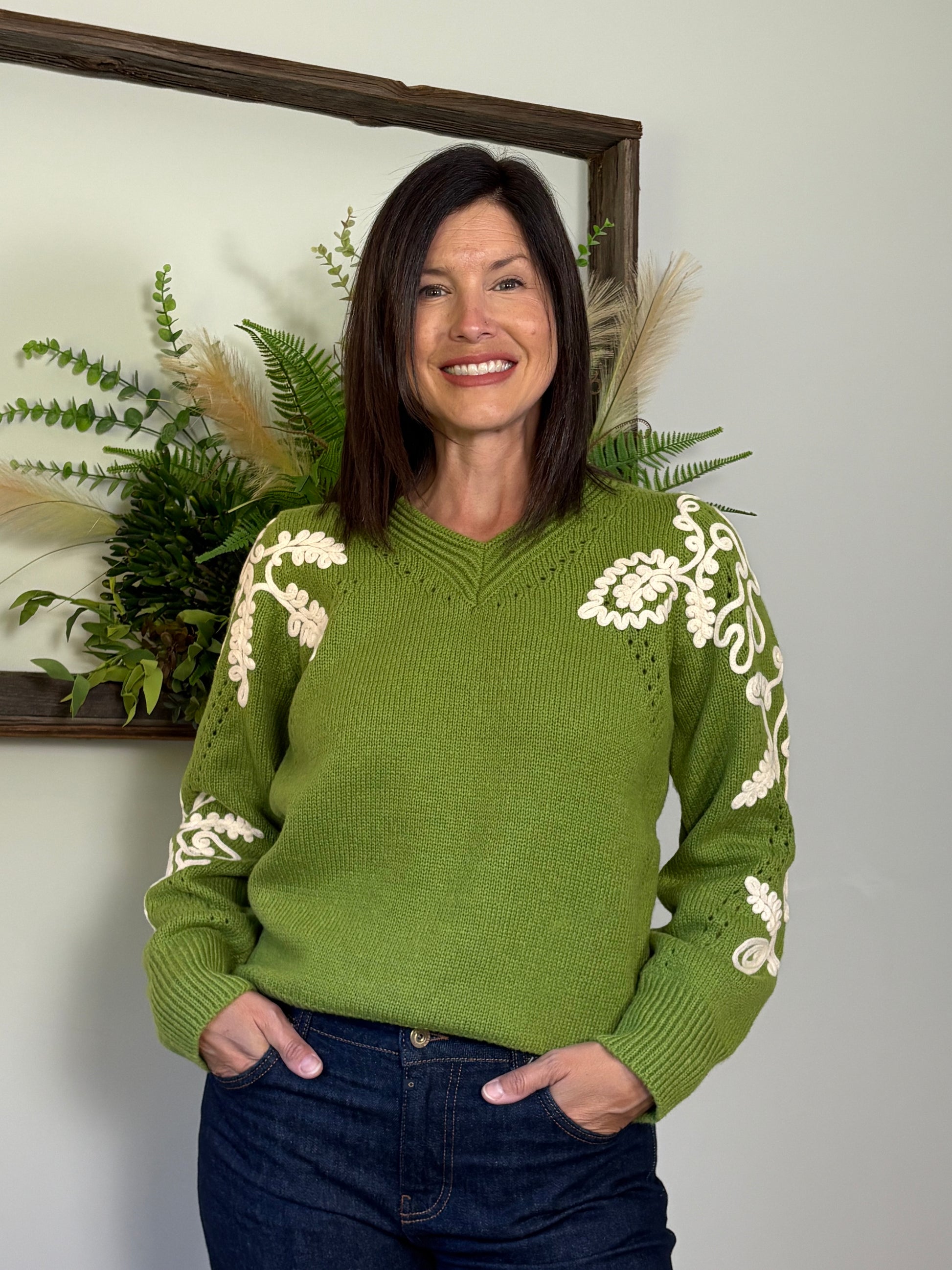 Woman wearing a green sweater with white patterns, standing against a neutral background.