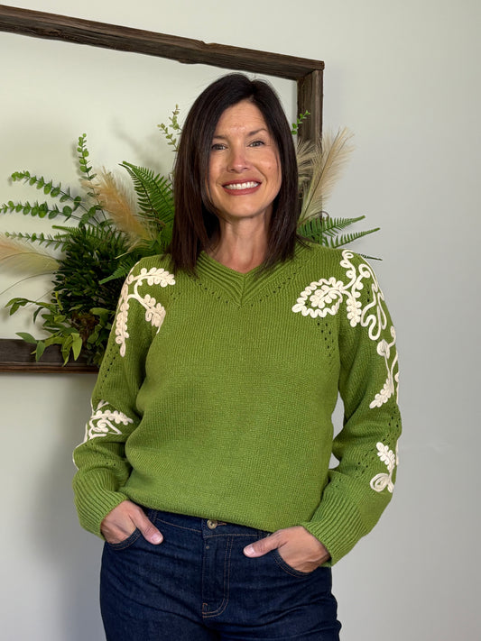 Woman wearing a green sweater with white patterns, standing against a neutral background.