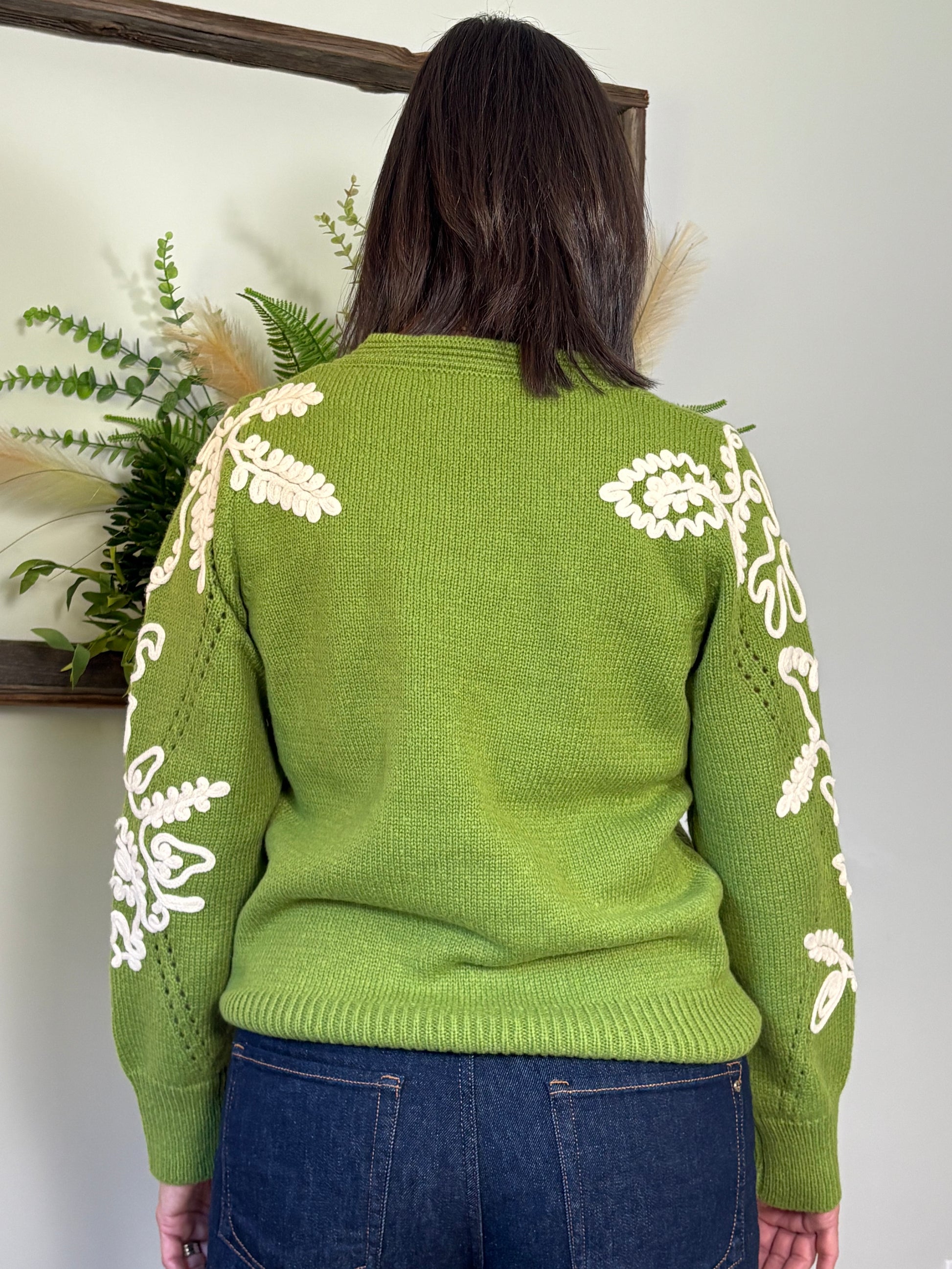 Person wearing a green sweater with white floral patterns, standing in front of a mirror.