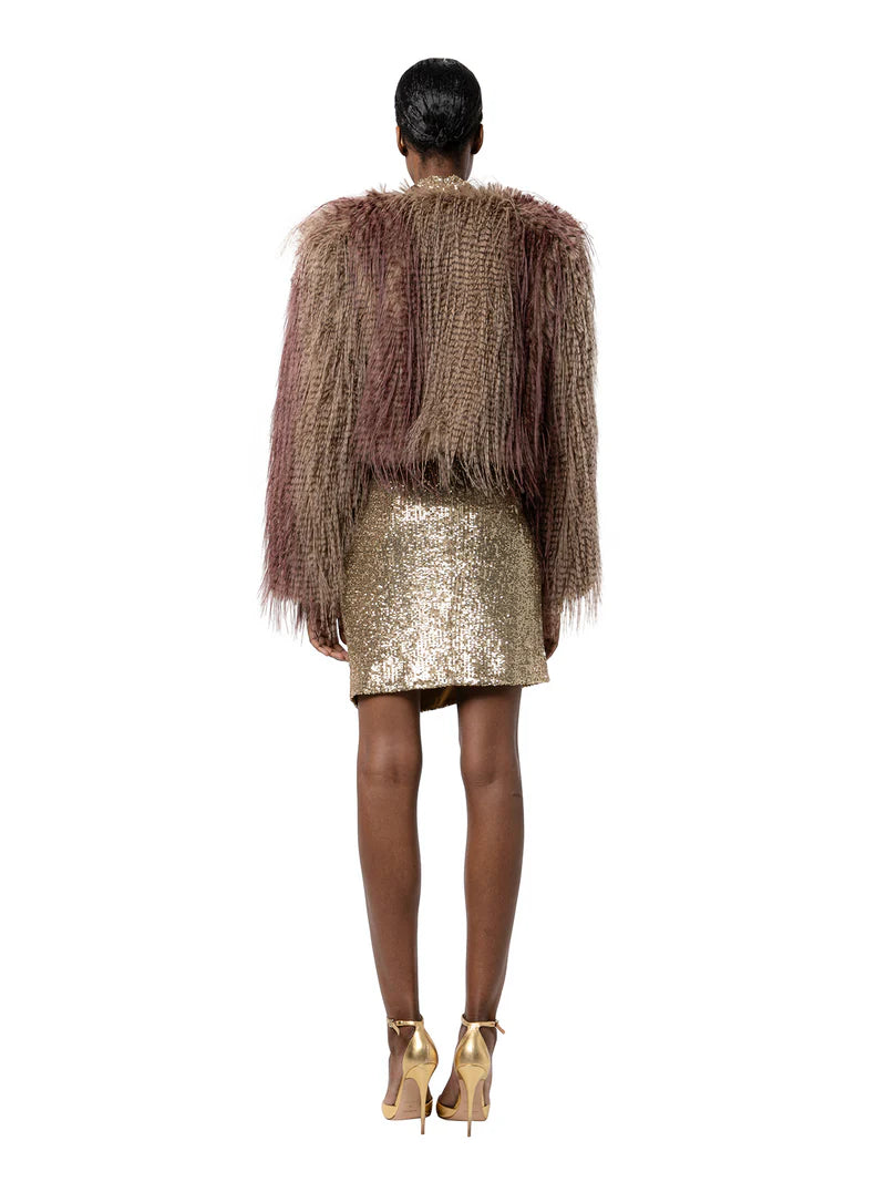 Person wearing a textured brown jacket and gold sequin skirt on a white background