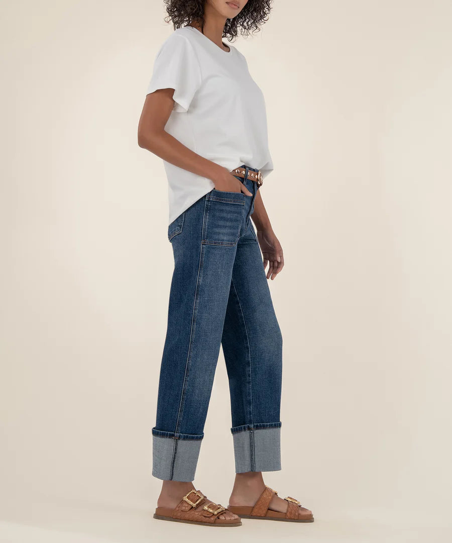 Person wearing a white t-shirt, blue jeans, and brown sandals on a beige background