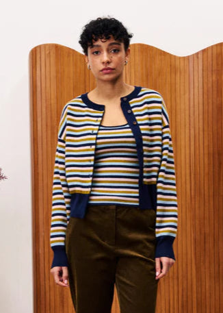 Person wearing a striped sweater and brown pants standing in front of a wooden screen.