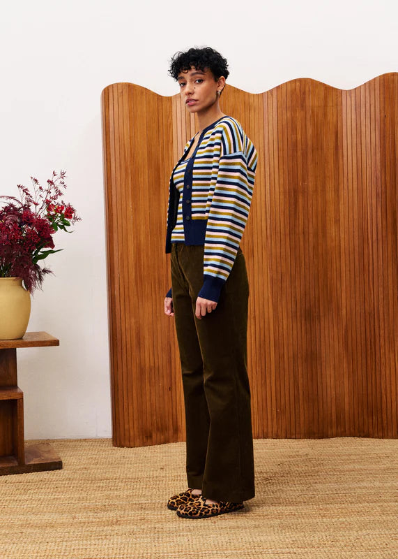 Woman wearing a striped sweater and green pants standing in front of a wooden screen.