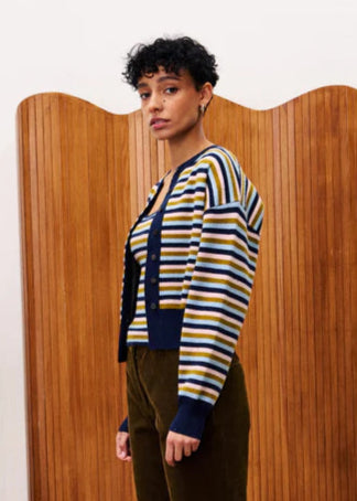 Woman wearing a striped sweater and green pants standing in front of a wooden screen.