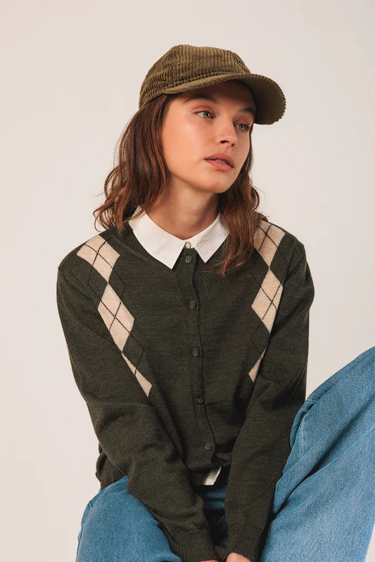 Person wearing a green argyle sweater and cap against a white background