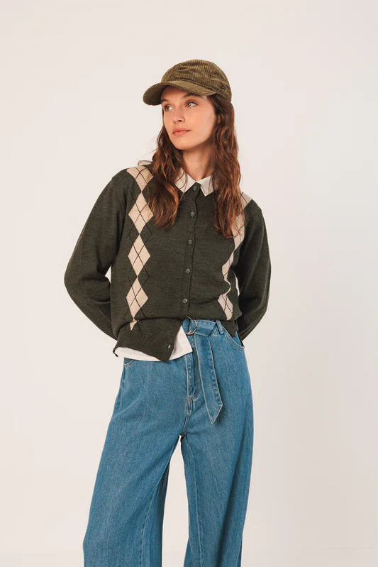 Person wearing a green argyle sweater, blue jeans, and a cap on a white background