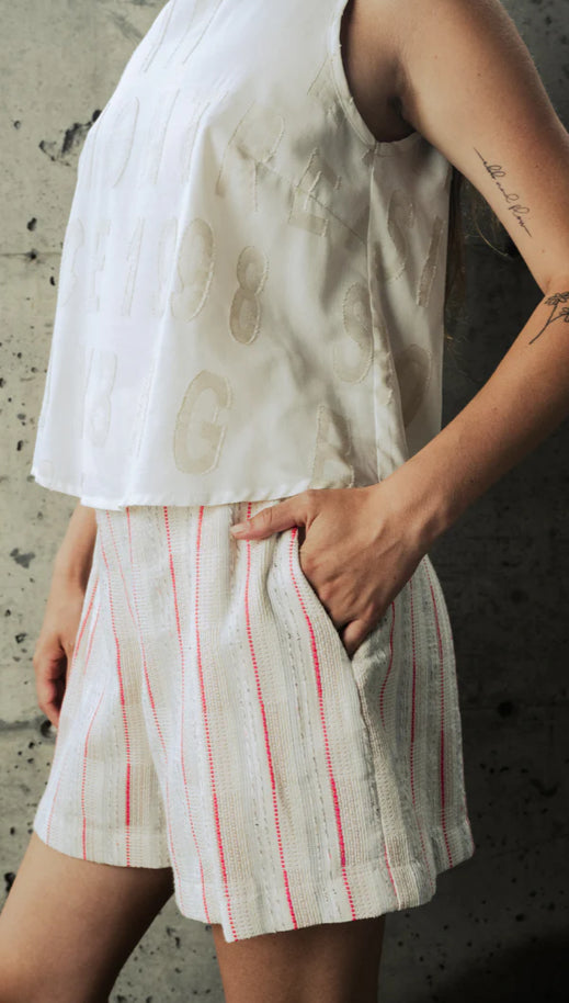 Introducing the Sao Paulo Shorts by BODYBAG By Jude, a chic addition to your summer wardrobe. These high-waisted shorts feature a flattering flared cut with front pleats and back darts for a stylish fit. They're designed with invisible zip and side pockets for convenience, along with a welt pocket at the back. Made from a beautiful fabric of creams with thread accents of bold right pink, custom woven in France, these shorts are both elegant and versatile, perfect for any occasion.