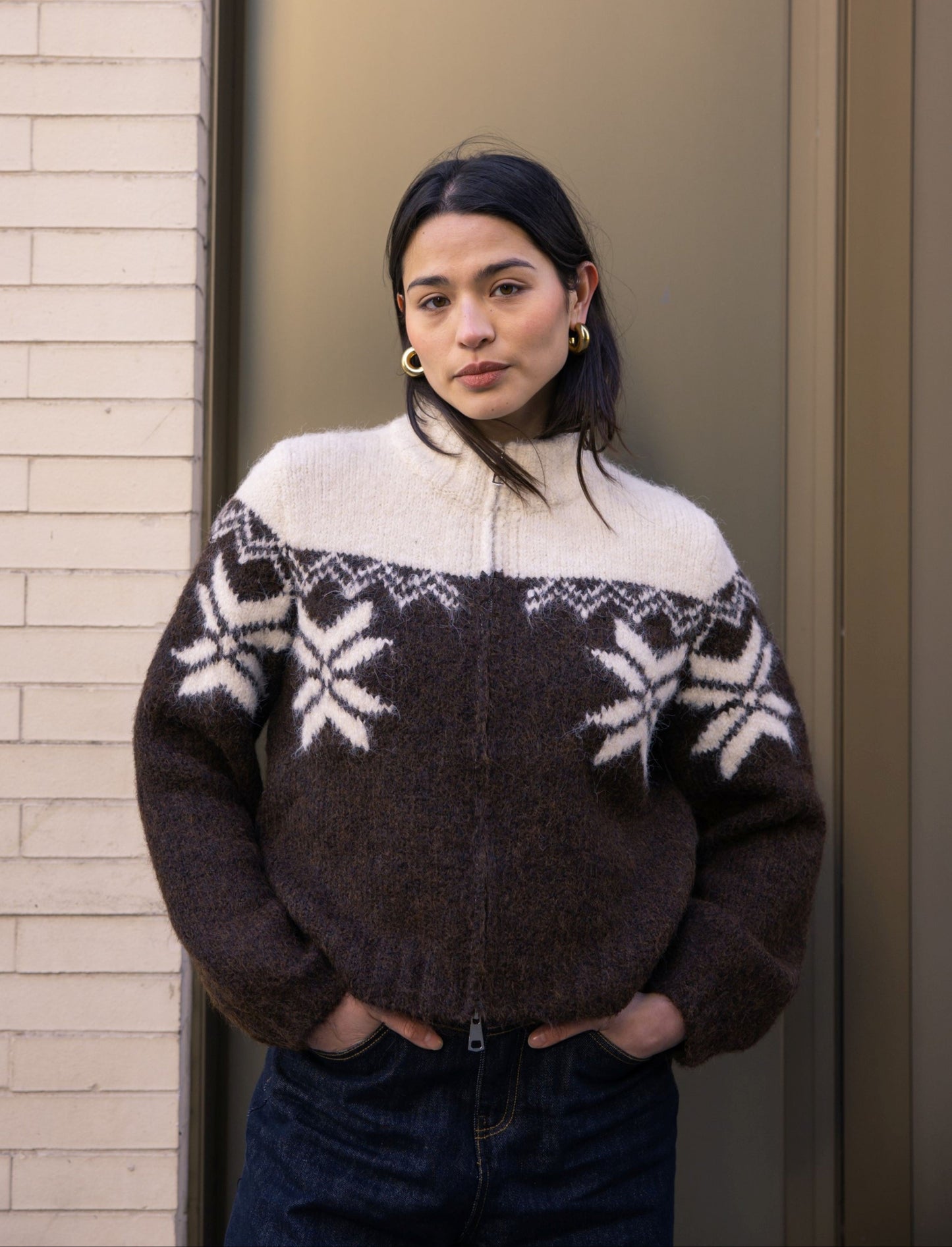 Person wearing a patterned sweater standing against a neutral wall.