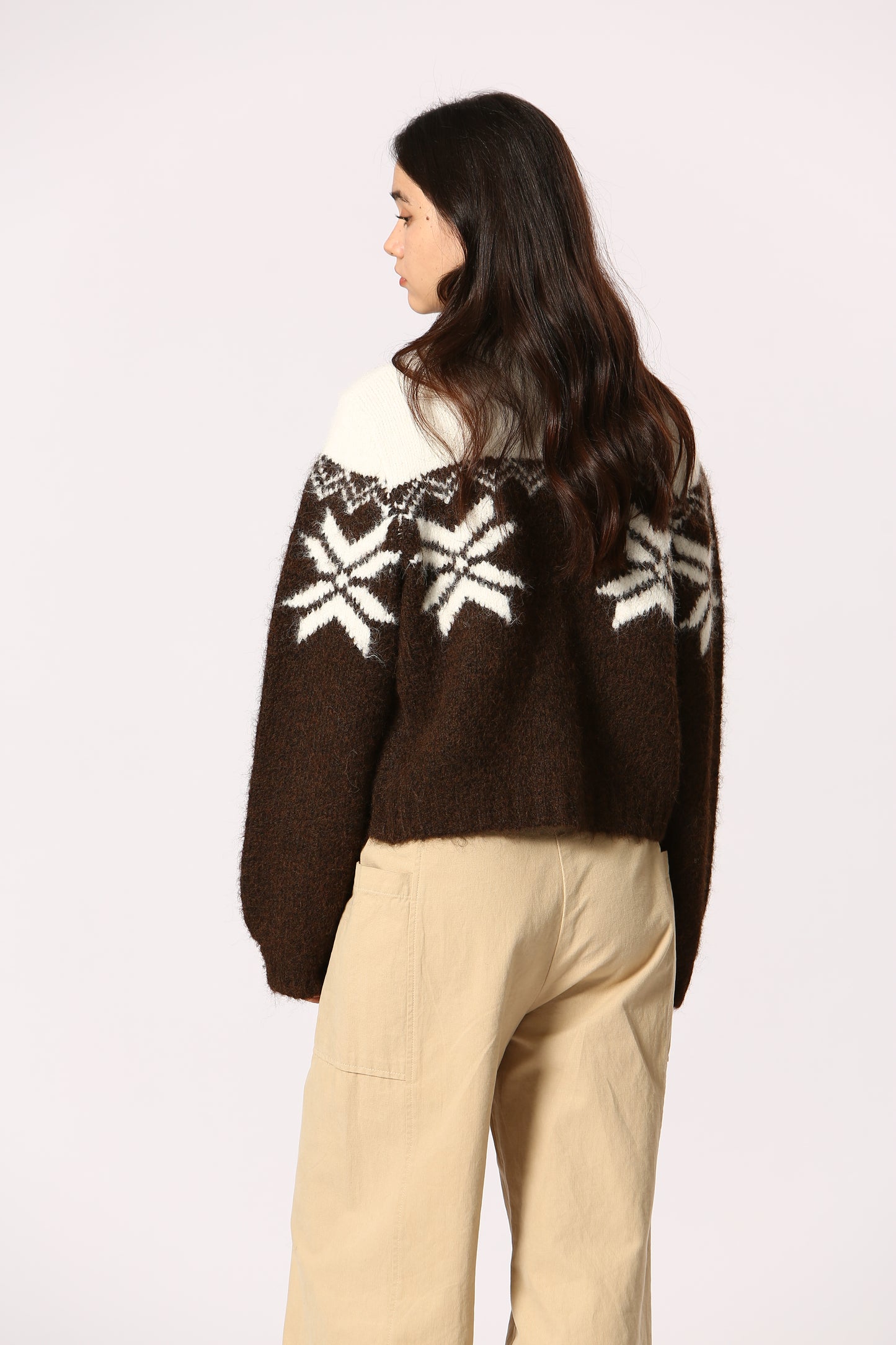 Brown sweater with white snowflake patterns worn by a person on a light gray background