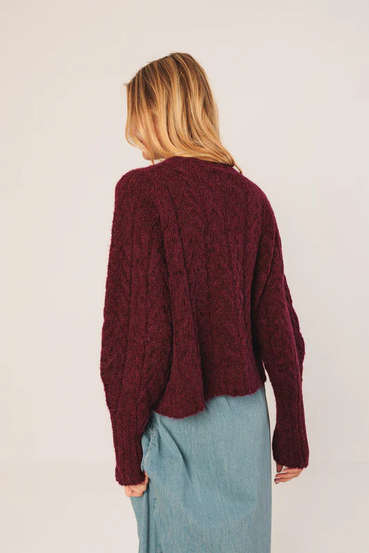 Person wearing a burgundy cable knit sweater with a plain background