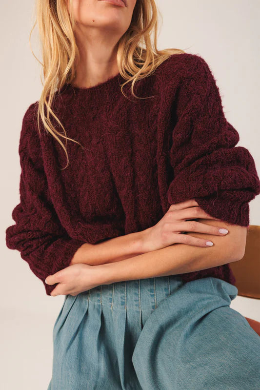 Person wearing a burgundy sweater and blue pants against a neutral background