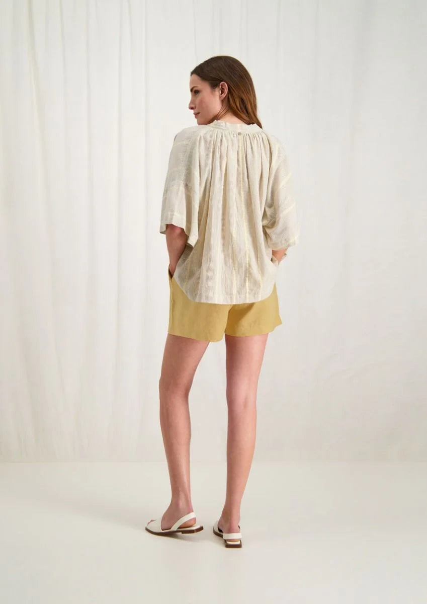 Introducing the Avril Blouse in Antique White by Circle of Trust. Made from soft 100% cotton, it's comfy and breathable for everyday wear. The loose fit and vertical stripe pattern give it a relaxed yet stylish vibe. With a V-neck and delicate strings, it's effortlessly charming. Plus, it has drop shoulders and wide sleeves for a comfy fit. Finished with tassel ties and subtle ochre accents, it's a versatile piece for any occasion. Pair it with denim shorts or a skirt for a casual look. 
