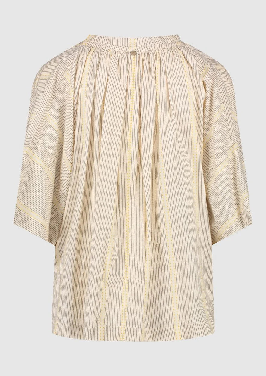 Introducing the Avril Blouse in Antique White by Circle of Trust. Made from soft 100% cotton, it's comfy and breathable for everyday wear. The loose fit and vertical stripe pattern give it a relaxed yet stylish vibe. With a V-neck and delicate strings, it's effortlessly charming. Plus, it has drop shoulders and wide sleeves for a comfy fit. Finished with tassel ties and subtle ochre accents, it's a versatile piece for any occasion. Pair it with denim shorts or a skirt for a casual look. 