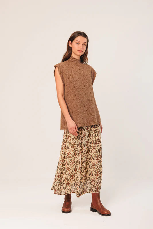 Woman wearing a brown sleeveless sweater and patterned skirt on a white background