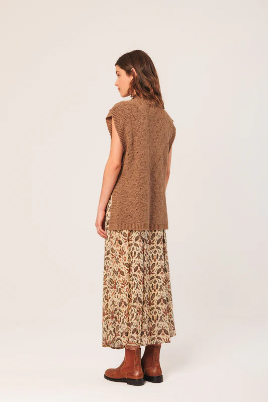 Woman wearing a brown sleeveless top and patterned skirt on a white background
