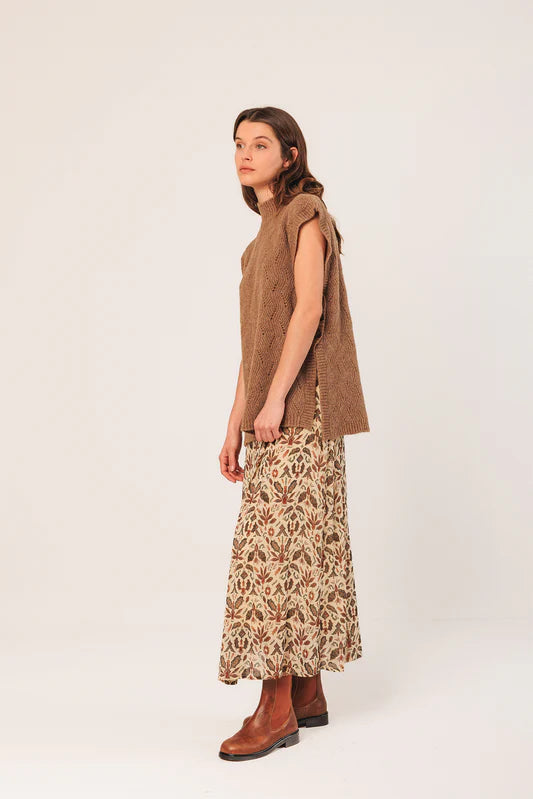 Woman wearing a brown sleeveless top and patterned skirt on a white background