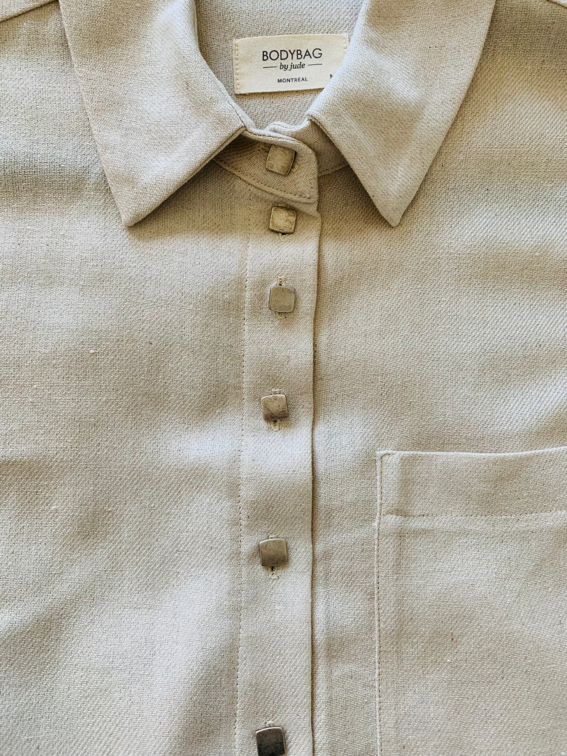 Effortlessly stylish and always on trend. Featuring a twist on the classic button-down style, the Douglas Top in a beautiful vanilla colour is a versatile addition to your wardrobe. Complete with our signature square matte metal buttons, one front pocket and a pleated back. This shirt is a must-have for any fashion-forward individual.