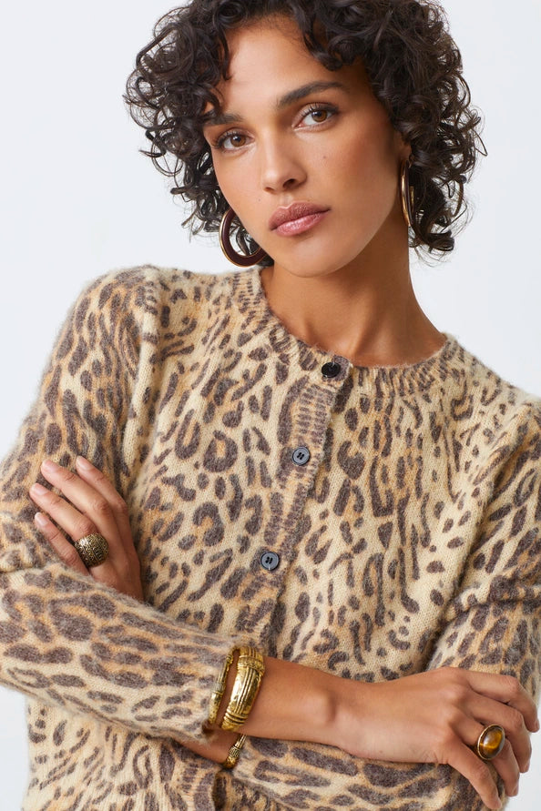 Woman wearing a leopard print cardigan with arms crossed on a light background