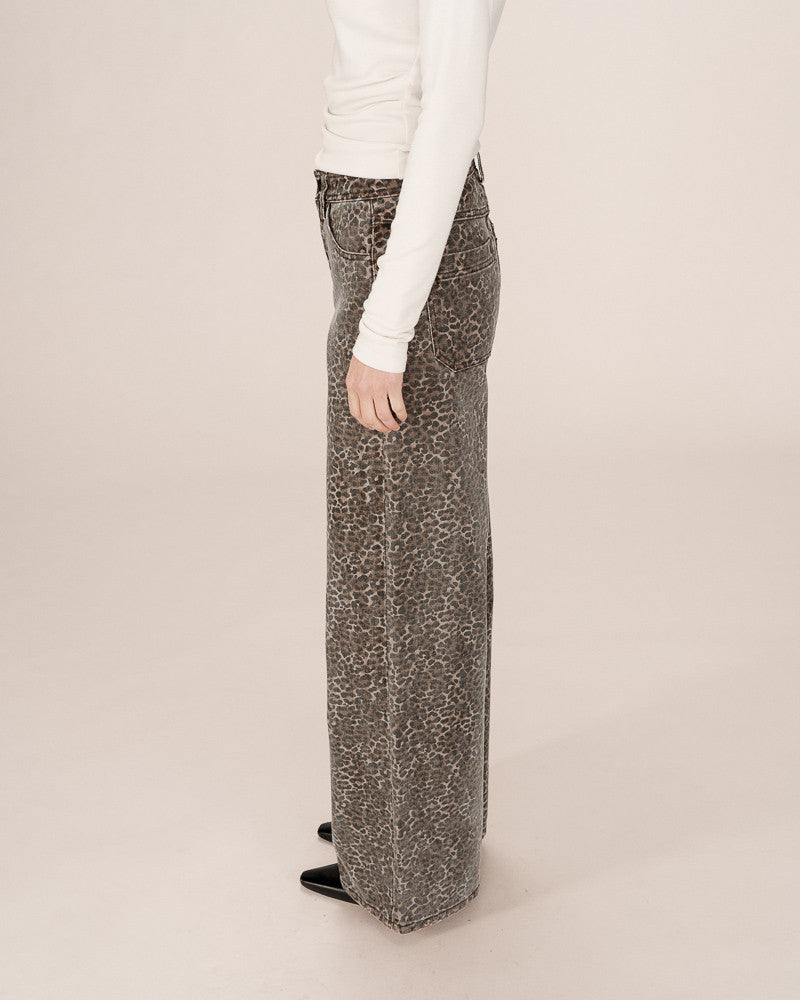 Person wearing a white long-sleeve top and leopard patterned wide-leg pants on a beige background