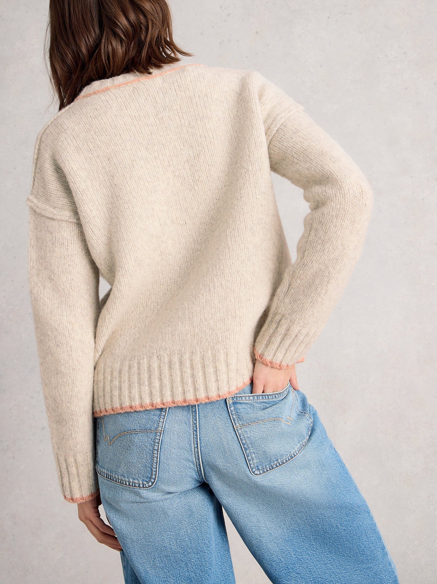 Person wearing a beige sweater and blue jeans against a plain background