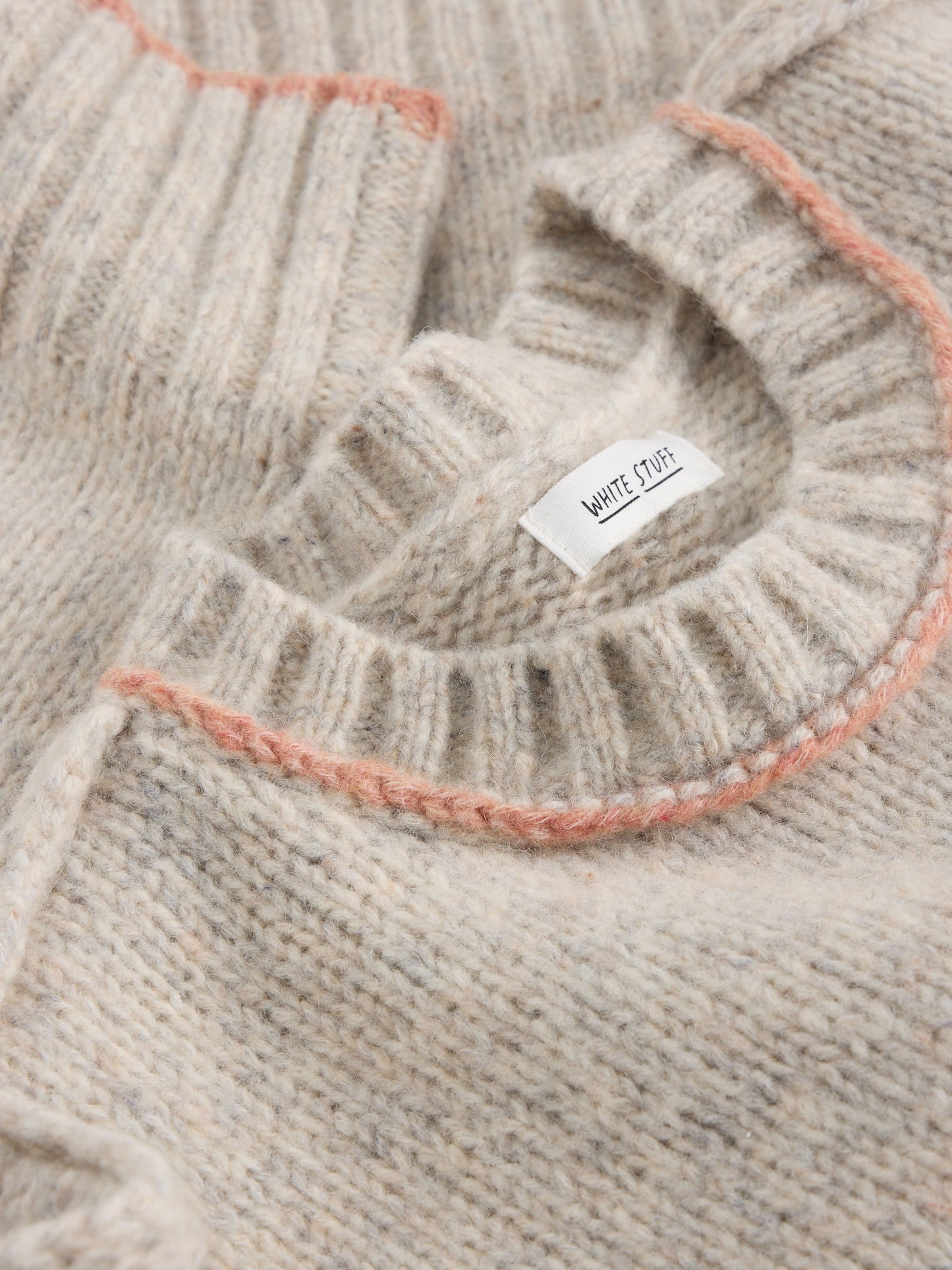 Close-up of a beige knit sweater with a brand label.