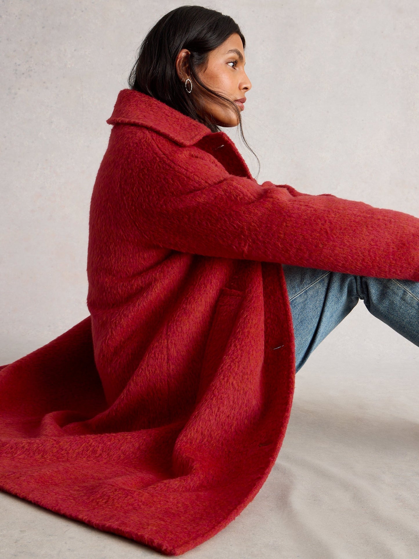 Person wearing a red coat sitting on a light-colored floor.