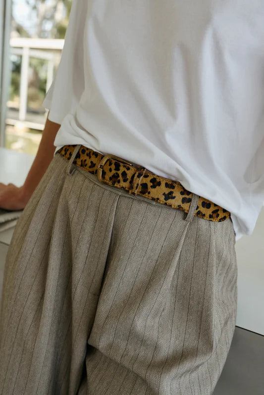 Person wearing beige pants with a leopard print belt and white shirt.