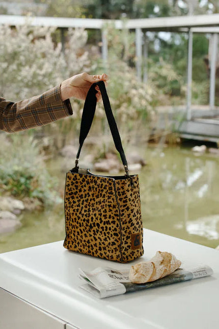 Person holding a leopard print handbag over a white surface with a blurred garden background