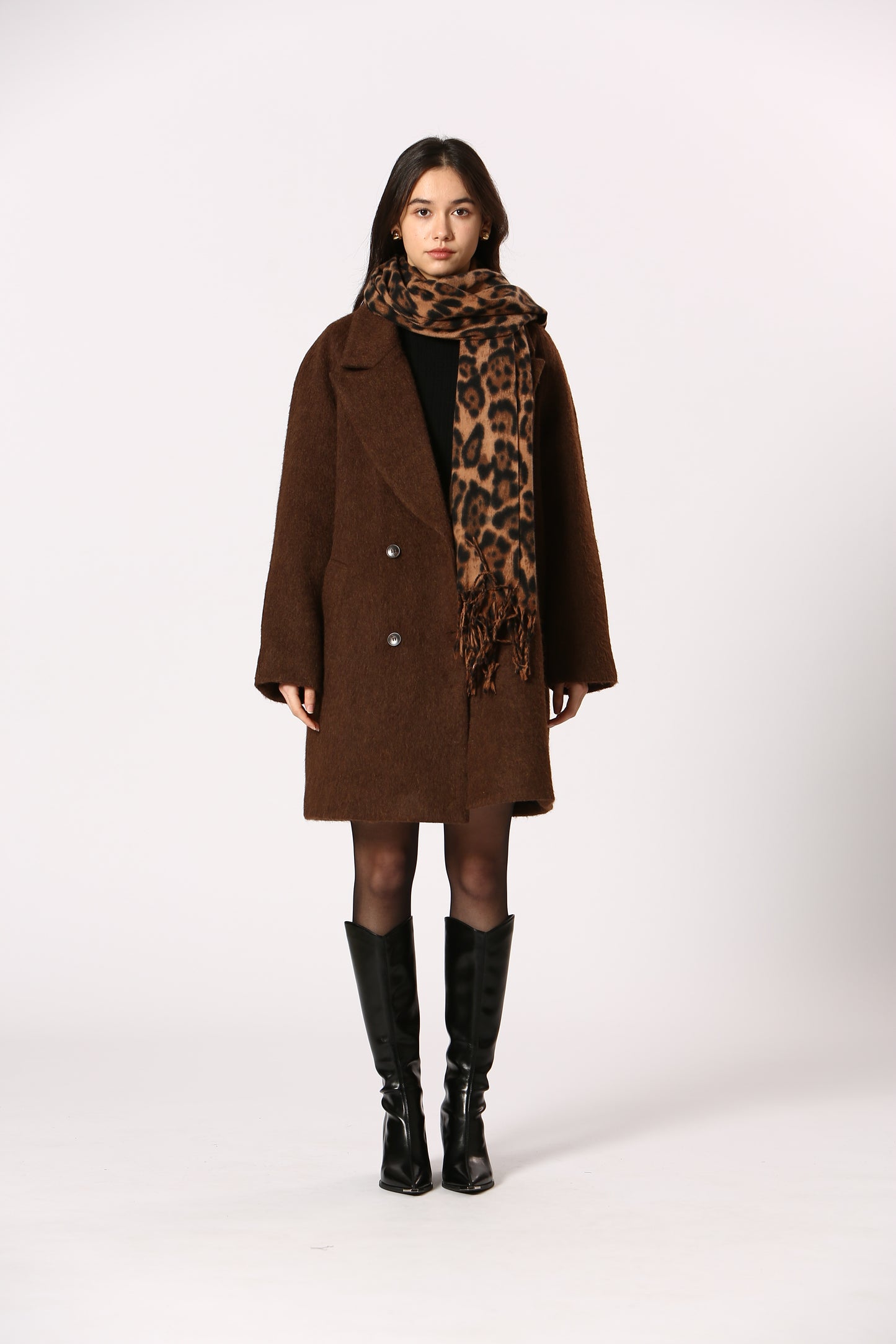 Person wearing a brown coat with leopard print scarf and black boots on a white background