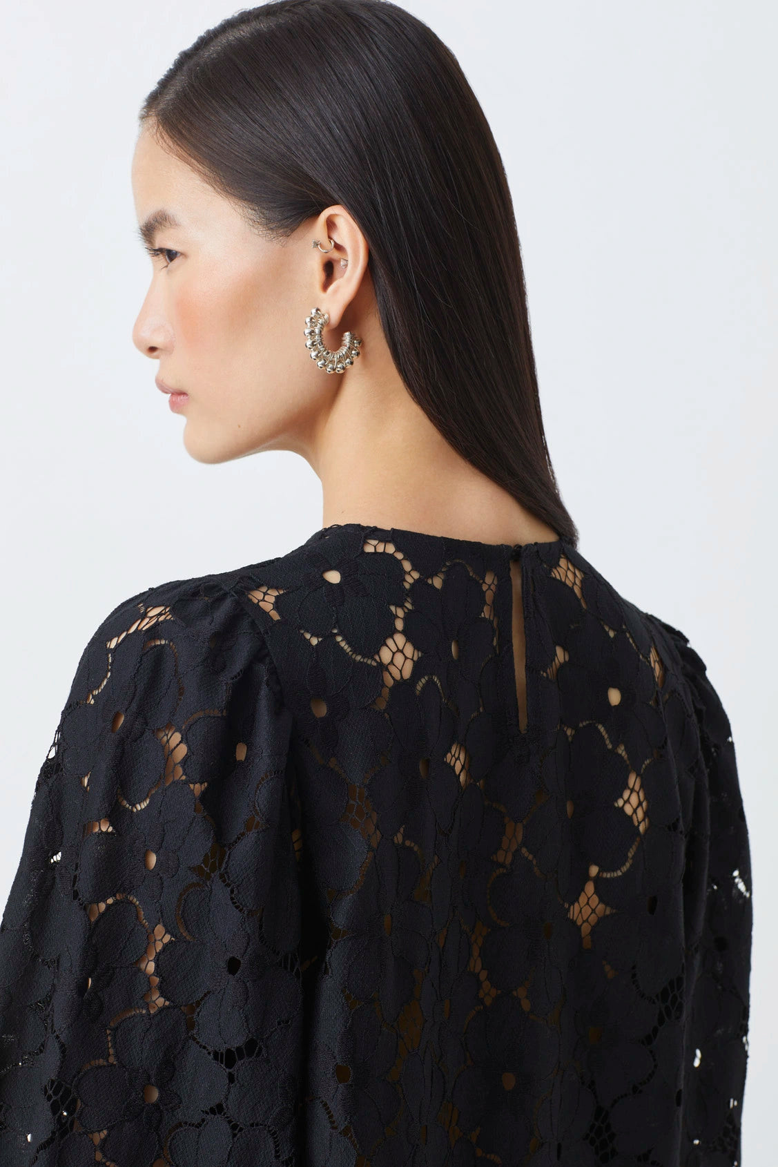 Woman wearing a black lace top with gold embroidery on a white background