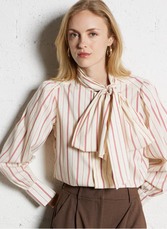 Woman wearing a striped blouse with a bow tie against a white wall